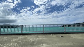 OKINAWA, JAPAN - AUG 2021 : Driving around Kouri Island bridge in sunny summer day. Wide camera, point of view (POV), seaside road driving. Japanese holiday, vacation and resort concept 4K video.