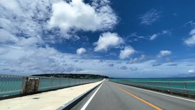 OKINAWA, JAPAN - AUG 2021 : Driving around Kouri Island bridge in sunny summer day. Wide camera, point of view (POV), seaside road driving. Japanese holiday, vacation and resort concept 4K video.