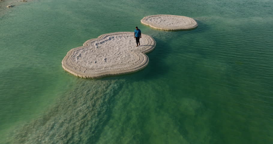 Man Standing On Mushroom Salt Formation Floating On The Dead Sea In Israel. aerial drone
