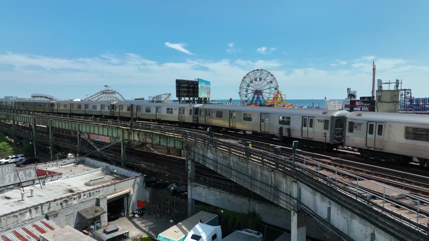 New York City , NY , United States - 06 13 2023: Aerial shot of NYC commuter train running on tracks in front of Coney Island amusement park. 