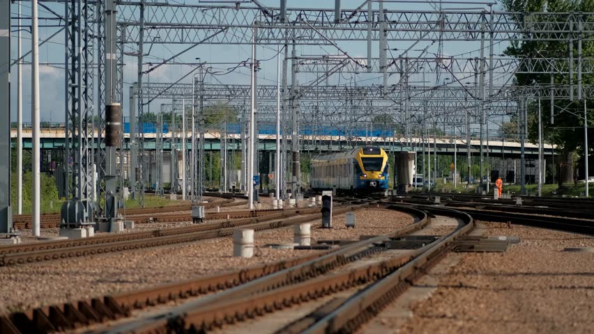 Blue and yellow train traveling through train station next to bridge.
