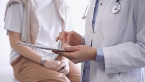 Doctor is using tablet computer while patient is sitting near. Unknown senior physician is at work. Medicine and health care concept