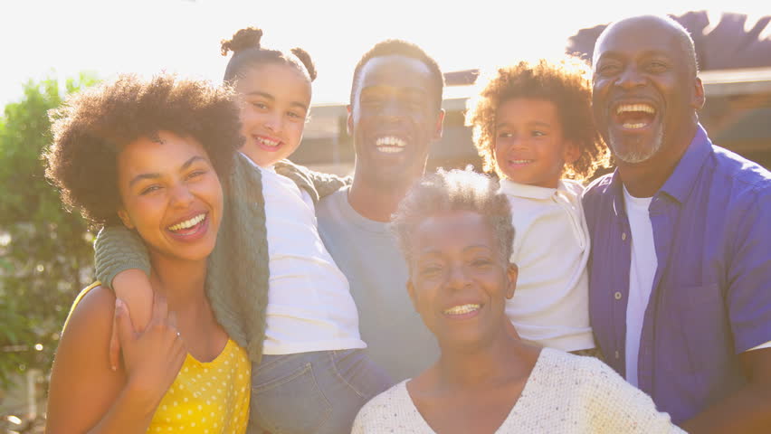 Multi-generation family at home in garden smiling into camera against flaring sun - shot in slow motion