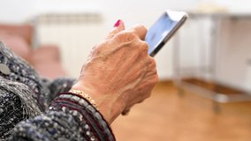 Elderly woman with smartphone, mobile phone in wrinkled female hands, close up. Concept of online communication in retirement. High quality 4k video