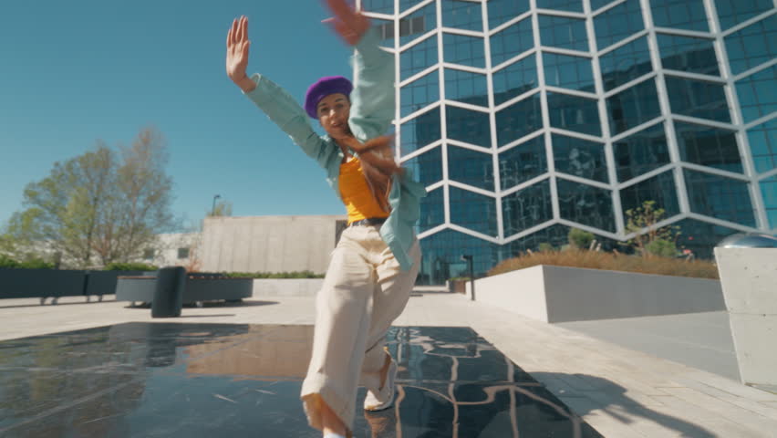 Young And Stylish Female Hip Hop Dancer Is Freestyling On City Street. Professional Newstyle Performer Doing Improvisation In Modern Urban Environment. Happy Caucasian Woman Practicing Choreography.