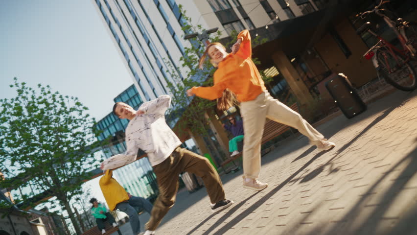 Two Professional Hip Hop Dancers Jamming On City Street Among Modern Buildings. Male And Female Newstyle Performers Freestyling Downtown, Stylish Friends Supporting, Livestreaming Via Smartphone.