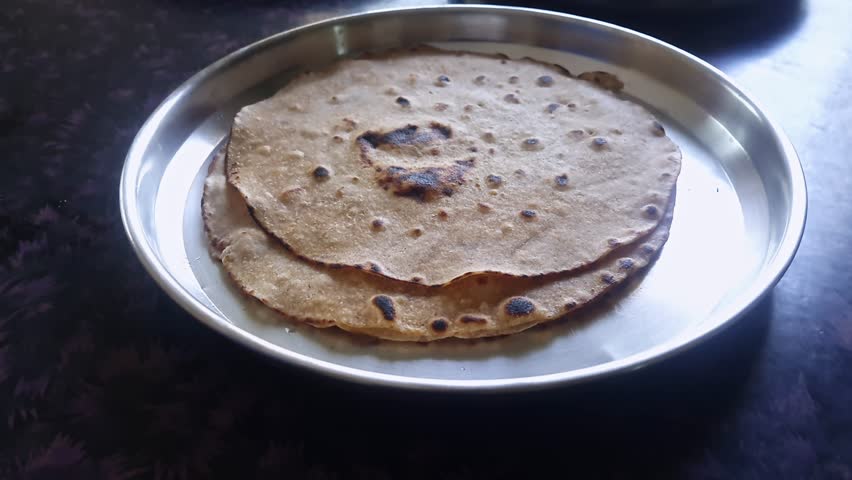 A silver plate on the table showcases a delightful homemade treat freshly made roti, chapati, or flatbread Royalty-Free Stock Footage #1105327477