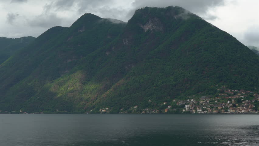 Sun beam slowing moving across mountain with small village at base of mountain on a lake