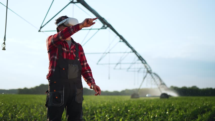 Agriculture.Farmer wearing virtual reality glasses in cornfield. Automatic watering system for plants in drought. Farmer irrigates green fields with help of modern technologies. Farm irrigation system Royalty-Free Stock Footage #1105333555