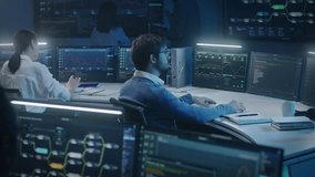 Software engineer works at computer in monitoring room late night. Big data scientists analyze server data. Multiple big screens on the wall with displayed real-time analysis charts. Cyber security. - Powered by Shutterstock - Get 15% off with code: PIKWIZARD15