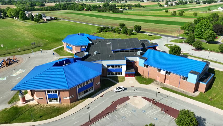 Birds-eye view of American Elementary School, panoramic wide shot. Aerial orbit around rural school with blue roof.