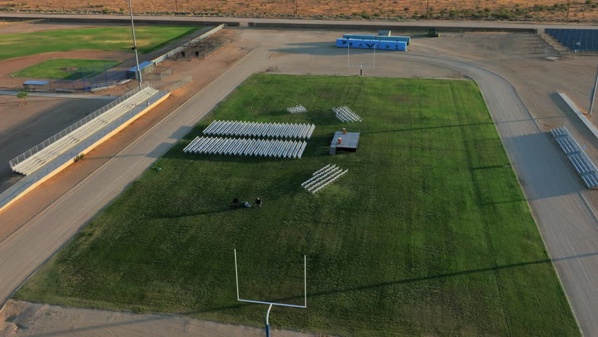 High school football and track field and bleachers set up for a graduation ceremony - aerial orbit 