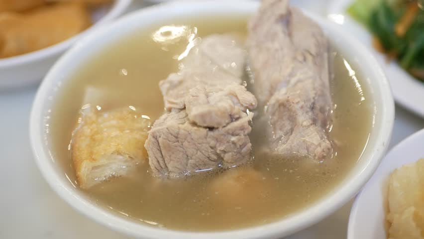 using chopsticks to grab pork rib from a bowl of bak kut teh with hot soup in lunch dinner meal time. Hot soup in asian singapore malaysia style. Tradition culture asian singaporean food Royalty-Free Stock Footage #1105339853