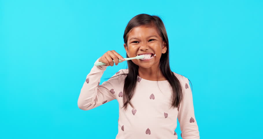 Child brushing teeth with smile, thumbs up in studio and morning routine for clean mouth, growth and happiness. Dental care, yes and face of happy girl on blue background, cleaning care and children Royalty-Free Stock Footage #1105340823