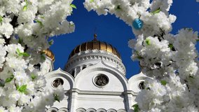 View of Cathedral of Christ the Saviour in Moscow, Russia through frame of white blooming flowers. Clear blue sky. Slow motion video. Easter holiday theme.	