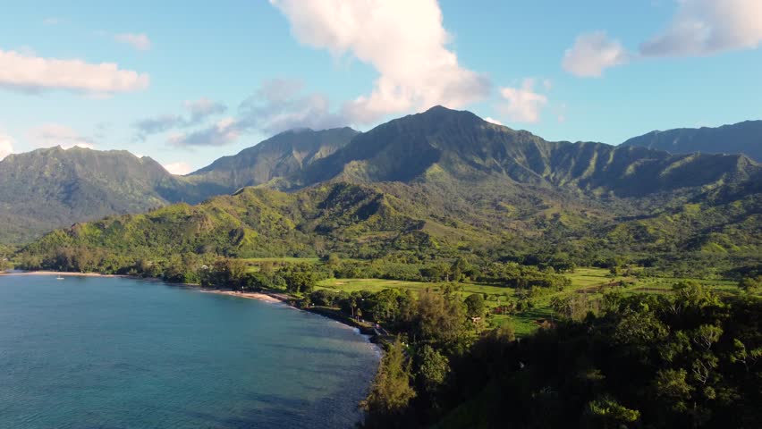 Cinematic Aerial shot of Hanalei Bay and green mountains, beach, boat, ocean with the Hanalei River near Princeville, Kauai, Hawaii