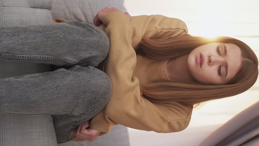 Vertical video. Teenager depression. Unhappy feelings. Sad disappointed girl sitting sofa leaning knees being frustrated light home interior. Royalty-Free Stock Footage #1105347795