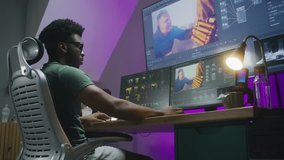 African American video editor makes color grading, works at home office. Computer and big digital screen with program interface with RGB tools and action movie footage. Film post production concept.