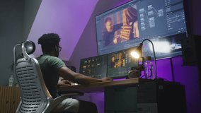 African American colorist, video editor makes color correction, works at home office. Computer and big digital screen with program interface and action movie footage. Concept of film post production.