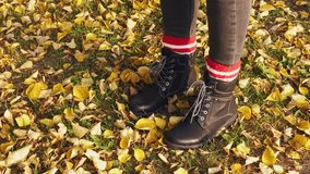 Partial view of woman in dark boots with striped red and white socks walking on path with golden leaves in autumn garden,shot in slow motion