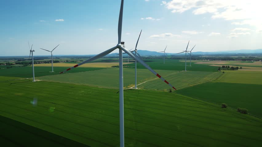 Group of windmills for electric power production in the green field against a blue sky. Aerial view of a large eco-energy wind farm. Environmental protection, renewable energy sources. 4k footage Royalty-Free Stock Footage #1105362229