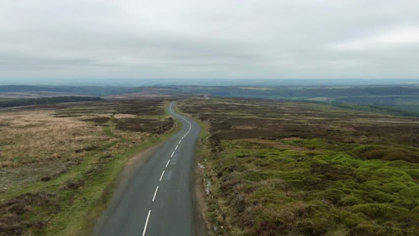 Drone flying over empty, twisty scenic driving road in the North Yorkshire Moors on a cloudy overcast day