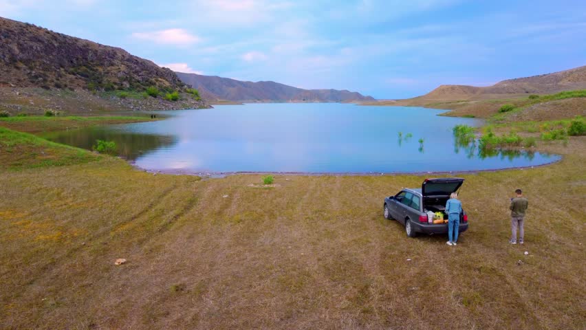 Happy family traveling by car for two. Rest on road by lake in mountains in Armenia. Spend night in nature and take break from hustle and bustle of city. Couple in car spoils everything.