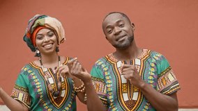 African couple dancing traditional dance. Man and woman in brightly ornamented clothing. Smiling male and female cheerfully moving against background of red wall. Multicultural woman in turban. - Powered by Shutterstock - Get 15% off with code: PIKWIZARD15