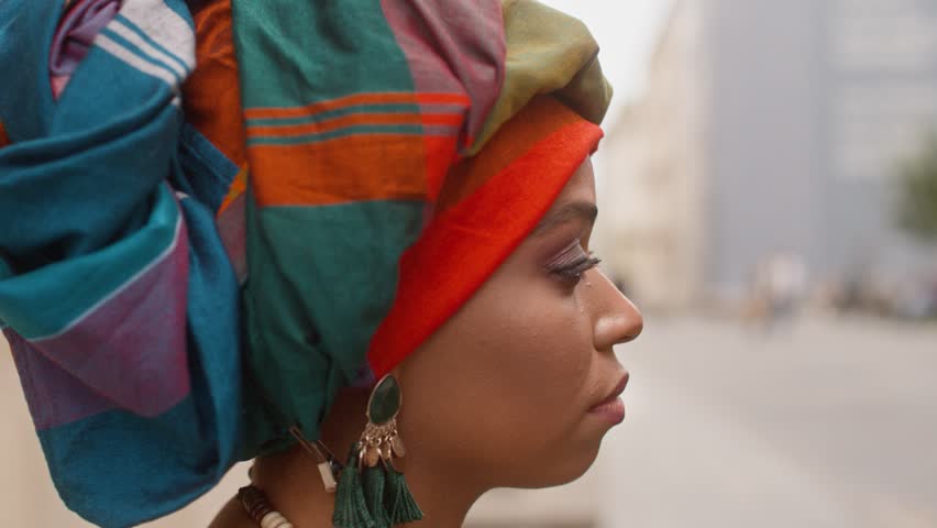 Shoot from side. Portrait of African woman. Serious female with turban. Close up of woman wearing colored scarf on head. Multiethnic woman in traditional jewelry and wrapped head. Ethnic diversity.