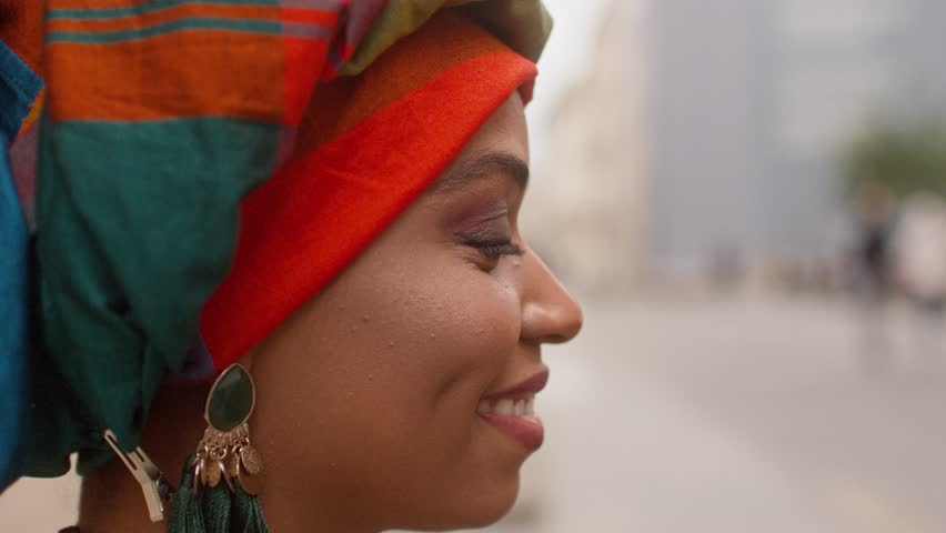Shoot from side. Portrait of African woman. Smiling female with turban. Close up of cheerful woman wearing colored scarf on head. Multiethnic woman in traditional jewelry and wrapped head.