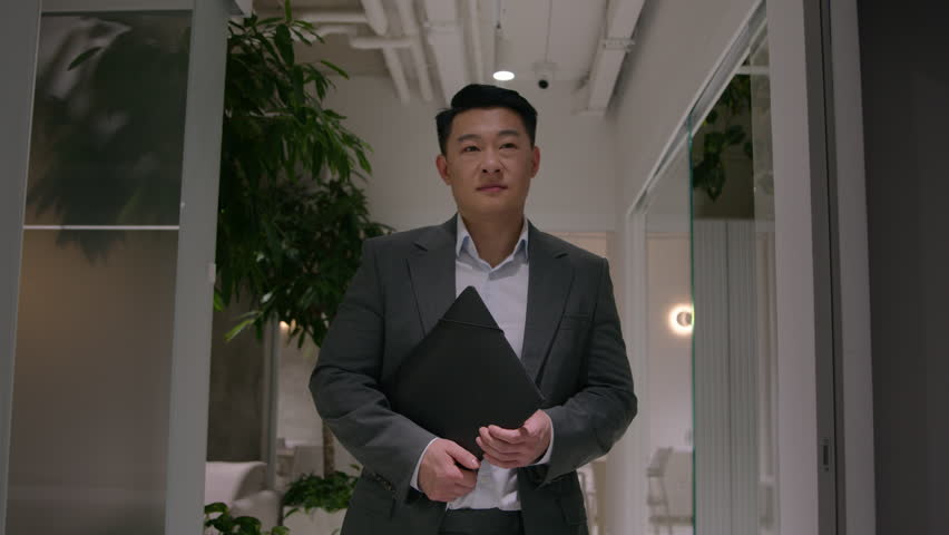 Happy Asian middle-aged businessman man walking in office hallway go to business meeting hold folder with documents smiling chinese male leader CEO company greet colleagues in corridor leave workplace Royalty-Free Stock Footage #1105372913