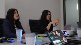 businesswomen conducting a business meeting in an office, woman CEO leader speaking with work team analyzing graphics on a tablet and using a projector on the table