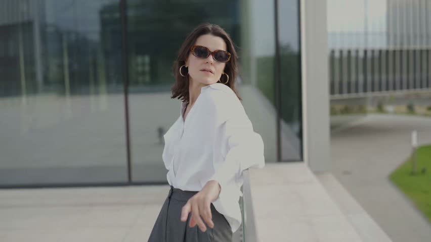 Young woman in a white shirt and glasses. Passes against the backdrop of blurred buildings.