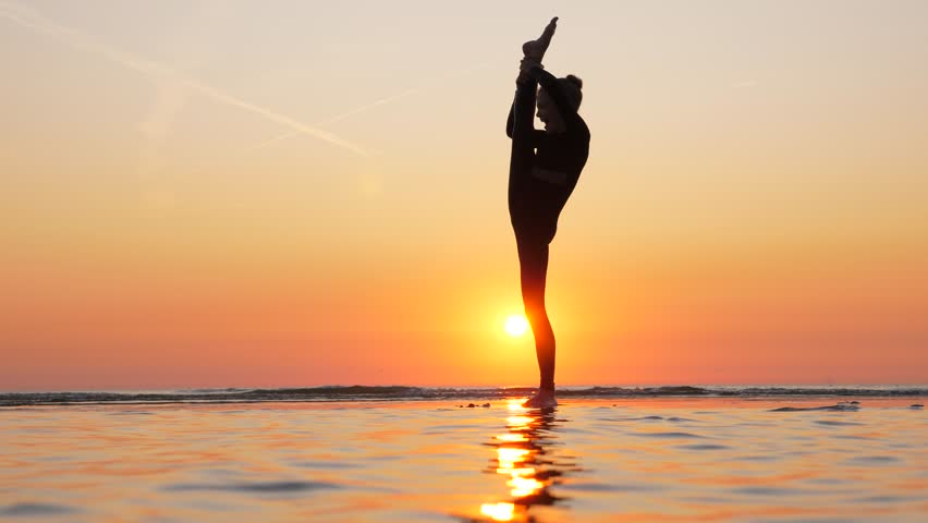 Young gymnast girl show standing front split, beautiful silhouette against sunset at sea beach. Professional teenager athlete demonstrate high skill and elegance | Shutterstock HD Video #1105379461