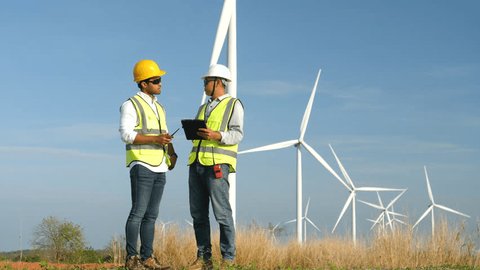 Slow motion, 4k footage, Team of male engineers working on site in wind turbine farm with clear blue sky on the background. Alternative energy, environmental friendly for the future. 库存视频