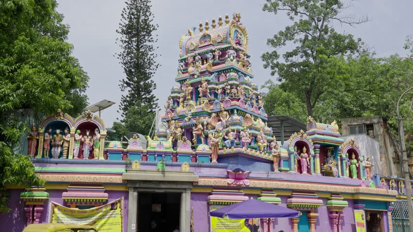 A wide view of a colorful Hindu temple with a shikhara adorned with sculptures of gods and goddesses amidst the Bangalore city