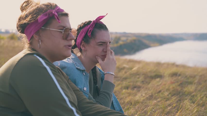 happy young women hikers talk spending time on steep river bank with grass in warm autumn evening close view