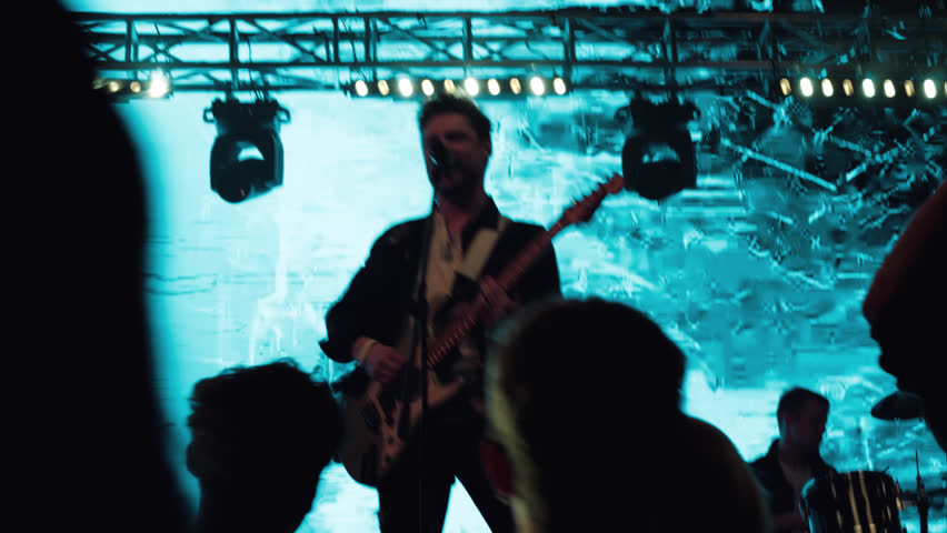 HANDHELD a rock band playing the gig during concert on stage of a large venue, surrounded by bright flashing stage lights