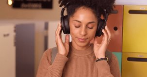 Young biracial female student dances with headphones in front of campus lockers