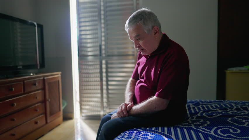 Religious Catholic senior man doing the sign of the cross in PRAYER sitting by bedside at home. Spiritual person having GRATITUDE and FAITH