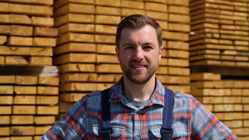 Young male worker in timber lumber warehouse. Wooden boards, lumber, industrial wood, timber. Pine wood timber