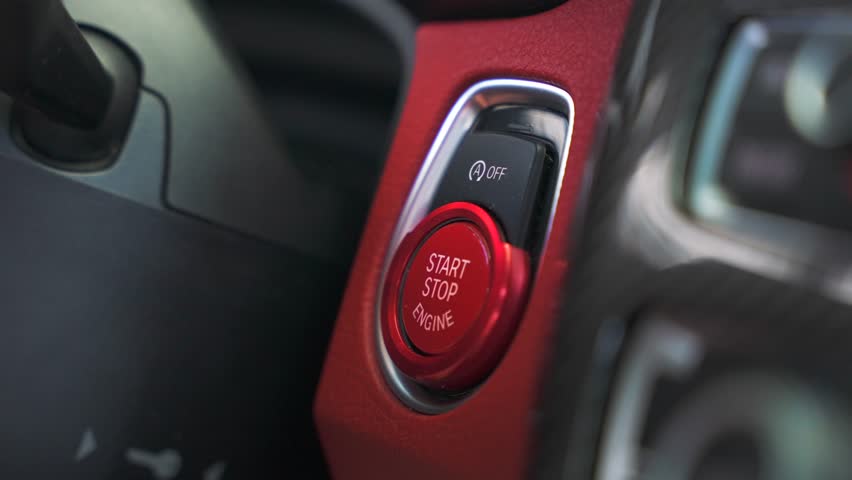 Man finger presses the red push start button in a sports car. Drive your dream vehicle on the high speed by the road
