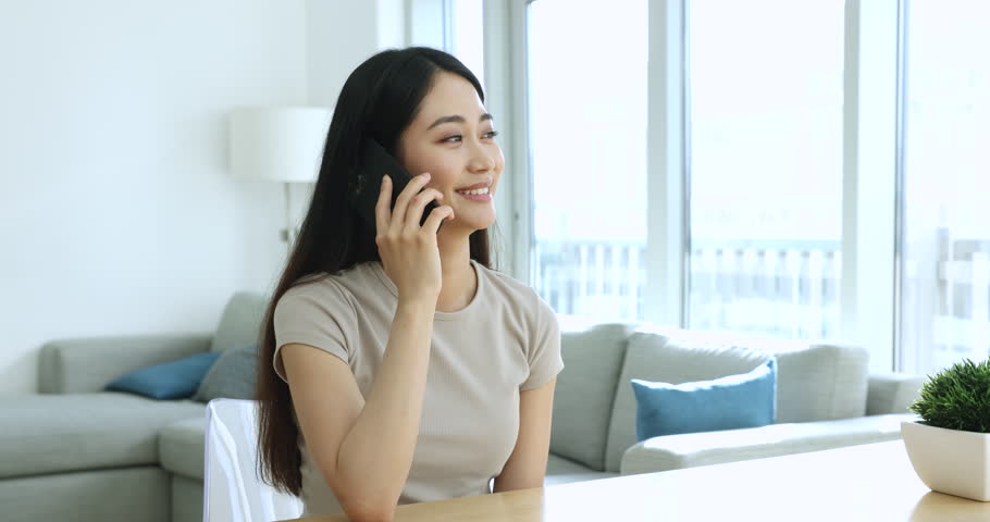 Pretty Asian woman lead pleasant conversation on phone, working in home office, provide information to client, enjoy personal talk to friend, share news speaking on cellphone. Communication use tech Royalty-Free Stock Footage #1105408735