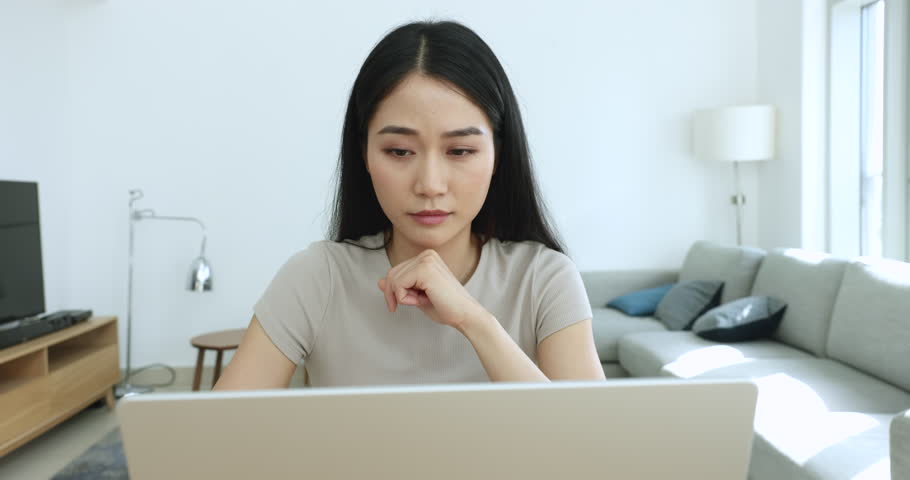 Focused Asian woman doing telecommute job, thinks over solution, search ideas engrossed in study, university exams preparation, making task, learn new program on laptop seated at desk in home office Royalty-Free Stock Footage #1105408755