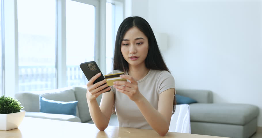 Young Asian woman hold credit card and smartphone frowning experiences problems with e-pay, feels annoyed due to lack of money, insufficient funds to buy on internet. Victim of fraud, scam, phishing Royalty-Free Stock Footage #1105412201