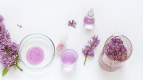 Using natural lilac flower extracts to develop new types of cosmetic products. Lilac fragrant extract in Petri dish, reagent solutions, sprig of lilac on laboratory table. Flat lay, close-up, video