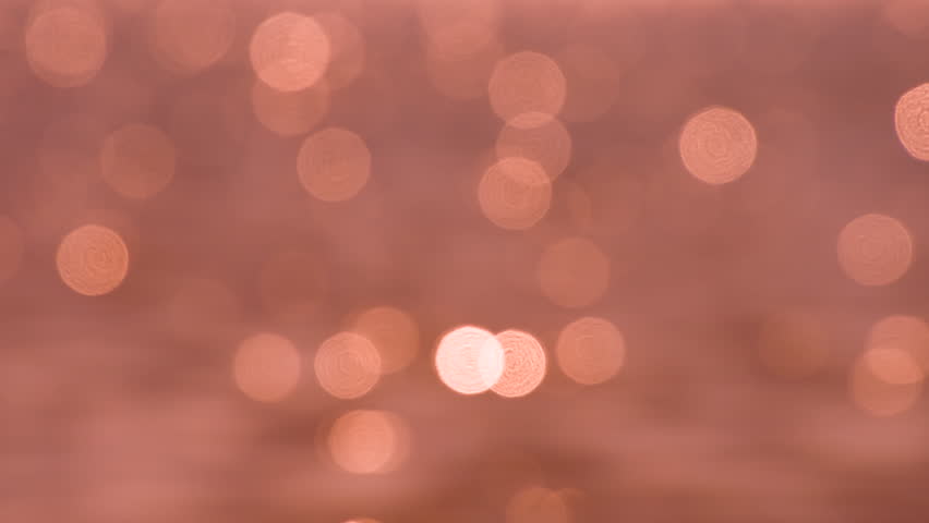 Glare of the Sea Surface at Sunset. Loop. Large glittering optical flares of bokeh on the gentle orange background of the midday sea