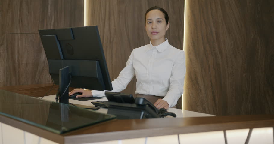Portrait of young Middle Eastern woman in uniform standing at hotel reception desk alone smiling looking at camera. Business locations and professions concept. Royalty-Free Stock Footage #1105422871