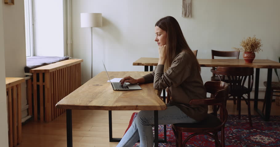 Attractive thoughtful woman sit at desk working remotely using laptop, ponder over on-line presentation or task, web surfing information spend time on internet, do freelance job or studying distantly Royalty-Free Stock Footage #1105424365