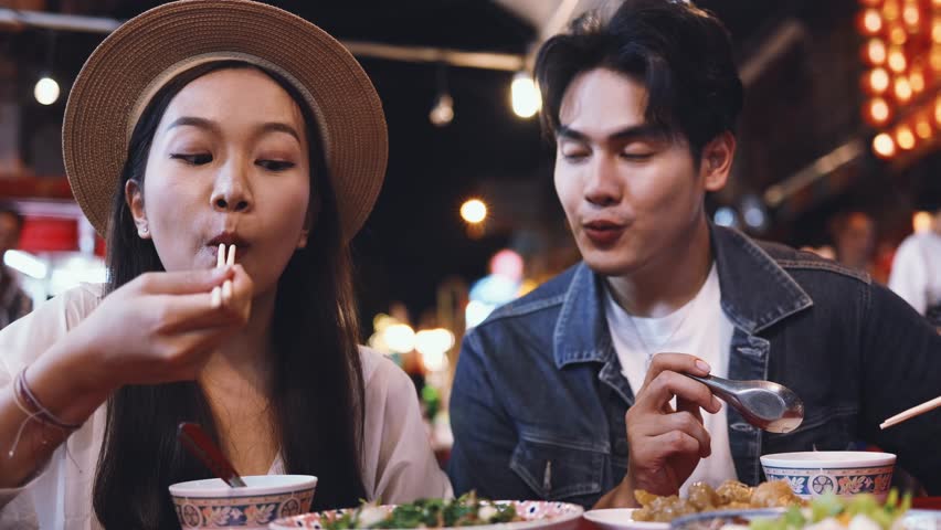 Young Asian couple traveler tourists eating Thai street food together in China town night market in Bangkok, Thailand